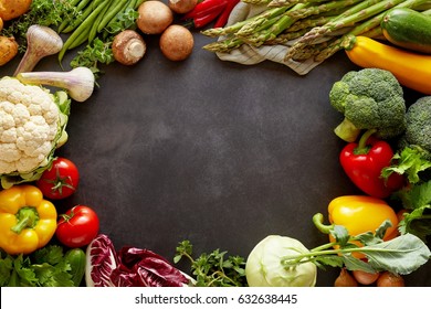 Healthy food background concept with fresh vegetables forming colorful frame around empty copy space of black chalkboard background in the middle, studio shot from above