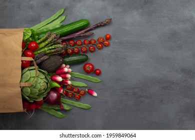 Healthy food background. Healthy food in paper bag, fresh vegetables on grey concrete table. Shopping vegetarian food supermarket concept. Top view. Green and red vegetables.