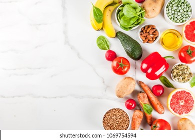 Healthy food background, trendy alkaline diet products - fruits, vegetables, cereals, nuts. oils, white marble background above copy space