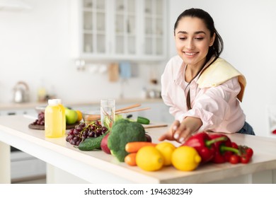 Healthy Food To Boost Your Immune System. Beautiful smiling young woman cooking fresh organic salad at home in modern kitchen, reaching for vegetables, copy space. Diet, Food And Lifestyle Concept