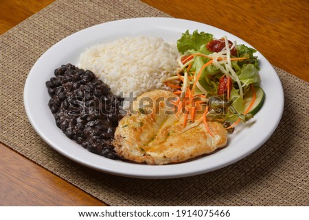 Healthy food with chicken breast, beans, rice, vegetable salad on a white plate on wooden table. Brazilian cuisine.