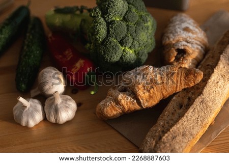 Healthy food composition with garlic, cucumber, red sweet pepper, broccoli, bread and croissant on a wooden table. View from above.