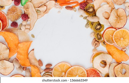 Healthy Food Concept. Frame Of Mixed Dried Fruit And Vegetable Chips, Candied Pumpkin Slices, Nuts And Seeds On White Marble Background With Blank Space For Text. Top View, Flat Lay.