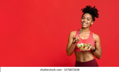 Healthy food concept. Happy African American Fitness Lady Eating Vegetable Salad, red studio background, panorama with copy space