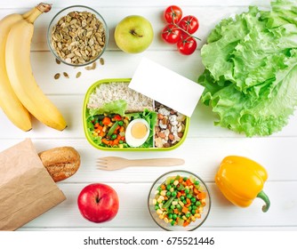 Healthy Food Concept: Lunch Box Filled With Rice, Mixed Vegetables, Boiled Egg And Nuts With Empty Card With Copy Space On White Wooden Background; Top View, Flat Lay