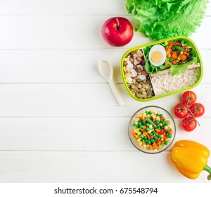 Healthy food concept: Lunch box filled with rice and mixed vegetables, boiled egg and snacks on white wooden background with copy space; top view, flat lay