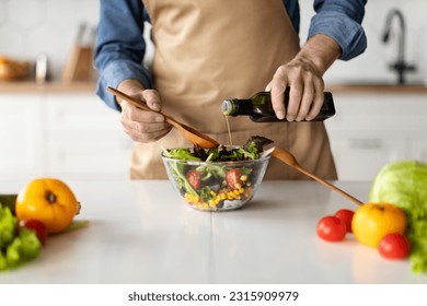 Healthy Food Concept. Mature Man Seasoning Vegetable Salad While Cooking In Kitchen, Unrecognizable Male Chef In Apron Preparing Vegetarian Meal At Home, Adding Olive Oil, Cropped Shot - Powered by Shutterstock