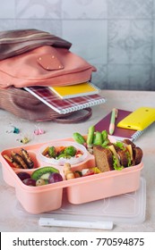 Healthy Food Concept: Open Lunch Box With Sandwiches, Vegetable Salad, Fresh Grape And Kiwi, Rice With Grilled Brussels Sprouts And Nuts On The Table Near School Backpack; Selective Focus