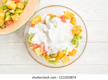 healthy food concept. summer fruit. fruit salad in a bowl with yoghurt on white wooden background flat lay top view