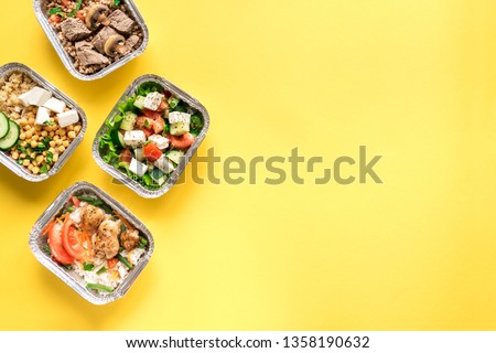 Healthy food delivery. Take away of organic daily meal on yellow, copy space. Clean eating concept, healthy food, fitness nutrition take away in foil boxes, top view.