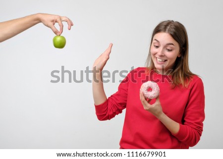 Healthy food and diet concept. Beautiful young woman choosing between fruits and sweets. She prefer a pink donut instead of green apple