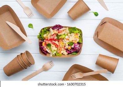 Healthy food in disposable eco friendly food packaging. Vegetable salad in the brown kraft paper food containers on white wooden background. Top view, flat lay.