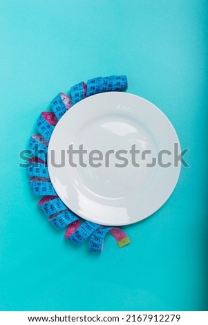  Healthy food, fitness for weight loss. Diet menu Obesity An empty plate with a measuring tape in centimeters on a blue background from above. . Place for an inscription. Advertising.