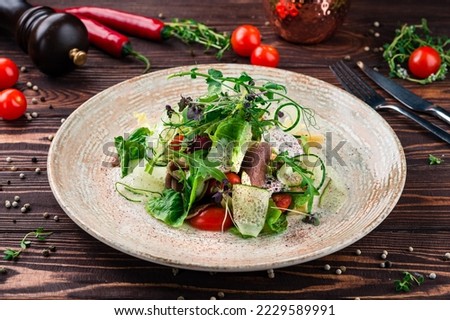 Healthy food, fresh green salad. Fresh green salad with beef tongue, cheese, olives, cucumbers, lettuce, cherry tomatoes, arugula and spices.
