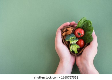 Healthy Food For Heart On Green Background. Man Hands Hold Plate With Vegetables, Spinach And Nuts. Diet, Superfood And Health Concept. Top View, Flat Lay, Copy Space