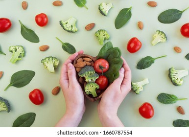 Healthy Food For Heart On Green Background. Womans Hands Hold Plate With Vegetables, Spinach And Nuts. Diet, Superfood And Health Concept. Top View, Flat Lay