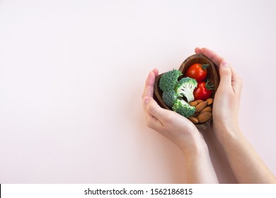 Healthy food for heart on light background. A plate with vegetables and nuts in a woman's hands. Diet and medicine concept. Top view, copy space - Powered by Shutterstock