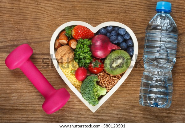 Healthy food in heart shaped bowl, bottle of\
water and dumbbell. Food such as blueberries, red onion,\
strawberry, parsley leaves, hazelnuts, walnut, tomato. kiwi,\
millet, buckwheat, radish,\
broccoli.