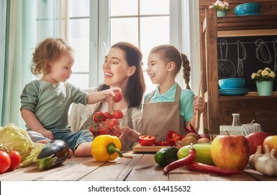 Healthy food at home. Happy family in the kitchen. Mother and children daughters are preparing the vegetables and fruit.