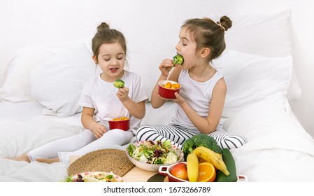 Healthy Food At Home. Happy Two Cute Children Eating Fruits And Vegetables In The Bedroom On The Bed. Healthy Food For Children And Teenagers.