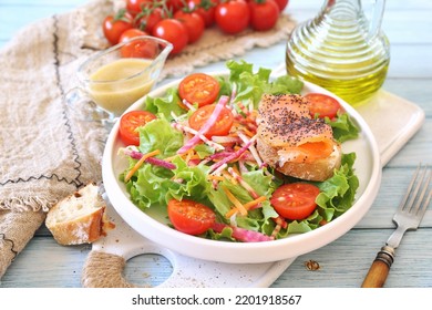 Healthy food. Lettuce salad with red fish, raw vegetables and olive oil. Red fish sandwich with rye bread, poppy seeds and mustard sauce on blue background