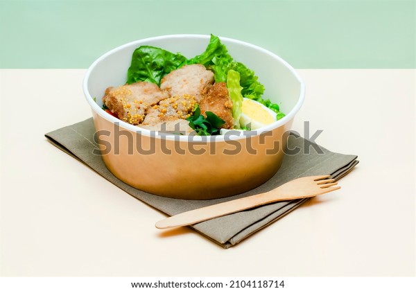 Healthy food lunch in kraft paper carton eco\
friendly box disposable bowl packaging container on green\
background. chicken, eggs, greens dinner. Take away delivery.\
environment protection