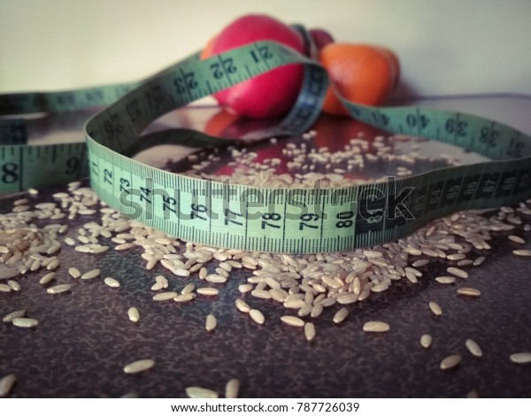 Healthy food option\
and weight management concept. Brown rice grains on the table with\
measuring tape and\
fruits.