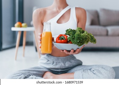 With healthy food and orange juice in hands. Young woman with slim body shape in sportswear have fitness day indoors at home.