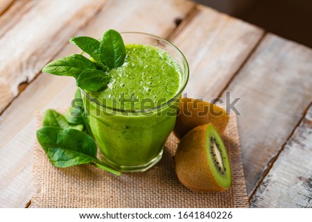Healthy food and vegan diet concept - glass of fresh green juice or smoothie with kiwi, spinach, banana, apple. Antioxidant detox beverage, raw ingredients.  Close up, wooden background, copy space