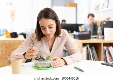 Healthy food in the workplace concept. Pretty hispanic woman eating a salad in the office.