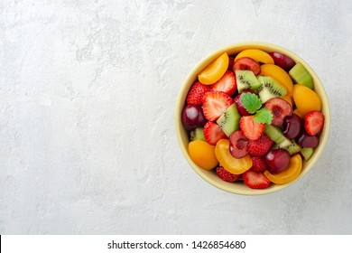 Healthy fresh fruit salad in bowl on gray concrete background. Top view. Copy space. - Shutterstock ID 1426854680