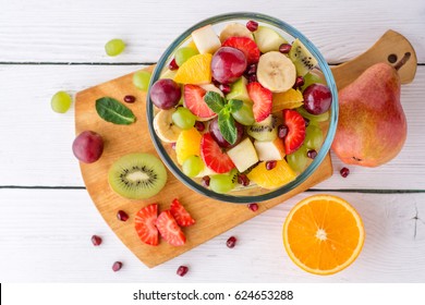 Healthy Fresh Fruit Salad In Glass Bowl On White Wooden Background. Top View.