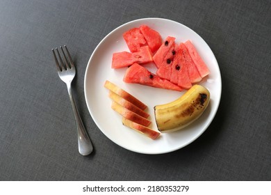 Healthy Fresh Fruit Salad In A White Plate On Black Background. Cut Fruit Plate Of Apple, Banana, And Watermelon Top View. Copy Space.