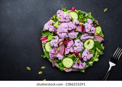 Healthy fresh vegan salad from purple cauliflower, cucumbers, red onion, radicchio, spinach with pumpkin seeds, dark table background, top view - Powered by Shutterstock