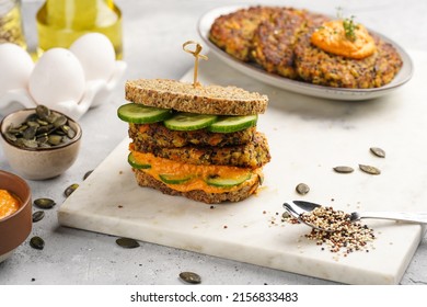 A Healthy Gluten-free Sandwich: Homemade Power Bread, Quinoa And Carrot Fritter, Orange Bell Pepper Hummus, Cucumbers, Sunflower Seeds On Marble Board