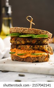 A Healthy Gluten-free Sandwich: Homemade Power Bread, Quinoa And Carrot Fritter, Orange Bell Pepper Hummus, Cucumbers, Sunflower Seeds On Marble Board