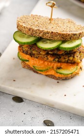 A Healthy Gluten-free Sandwich: Homemade Power Bread, Quinoa And Carrot Fritter, Orange Bell Pepper Hummus, Cucumbers, Sunflower Seeds On Marble Board