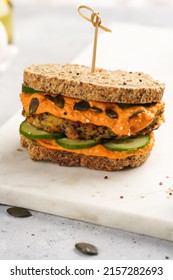 A Healthy Gluten-free Sandwich: Homemade Power Bread, Quinoa And Carrot Fritter, Orange Bell Pepper Hummus, Cucumbers, Sunflower Seeds On Marble Board