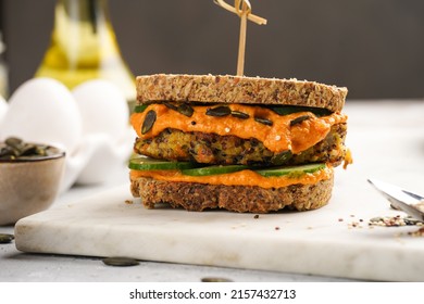 A Healthy Gluten-free Sandwich: Homemade Power Bread, Quinoa And Carrot Fritter, Orange Bell Pepper Hummus, Cucumbers, Sunflower Seeds On Marble Board