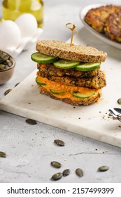 A Healthy Gluten-free Sandwich: Homemade Power Bread, Quinoa And Carrot Fritter, Orange Bell Pepper Hummus, Cucumbers, Sunflower Seeds On Marble Board