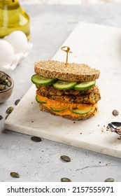 A Healthy Gluten-free Sandwich: Homemade Power Bread, Quinoa And Carrot Fritter, Orange Bell Pepper Hummus, Cucumbers, Sunflower Seeds On Marble Board