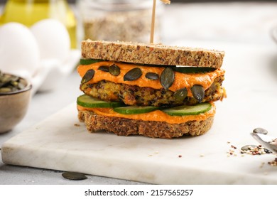 A Healthy Gluten-free Sandwich: Homemade Power Bread, Quinoa And Carrot Fritter, Orange Bell Pepper Hummus, Cucumbers, Sunflower Seeds On Marble Board