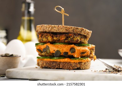 A Healthy Gluten-free Sandwich: Homemade Power Bread, Quinoa And Carrot Fritter, Orange Bell Pepper Hummus, Cucumbers, Sunflower Seeds On Marble Board