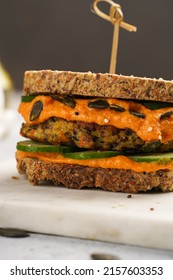 A Healthy Gluten-free Sandwich: Homemade Power Bread, Quinoa And Carrot Fritter, Orange Bell Pepper Hummus, Cucumbers, Sunflower Seeds On Marble Board