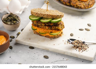 A Healthy Gluten-free Sandwich: Homemade Power Bread, Quinoa And Carrot Fritter, Orange Bell Pepper Hummus, Cucumbers, Sunflower Seeds On Marble Board