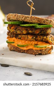 A Healthy Gluten-free Sandwich: Homemade Power Bread, Quinoa And Carrot Fritter, Orange Bell Pepper Hummus, Cucumbers, Sunflower Seeds On Marble Board