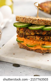 A Healthy Gluten-free Sandwich: Homemade Power Bread, Quinoa And Carrot Fritter, Orange Bell Pepper Hummus, Cucumbers, Sunflower Seeds On Marble Board