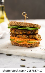 A Healthy Gluten-free Sandwich: Homemade Power Bread, Quinoa And Carrot Fritter, Orange Bell Pepper Hummus, Cucumbers, Sunflower Seeds On Marble Board