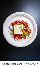 Healthy Greek Salad In Flat Lay On Black Table Surface.Delicious Mediterranean Snack Food Served On Recyclable Paper Plate.Good Food With Feta Cheese,olive Oil,peppers,red Onion Rings Shot From Above