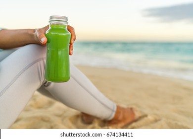 Healthy green juice detox smoothie drink beach woman. Girl holding glass bottle of cold pressed vegetable, juicing trend for nutrition cleanse.